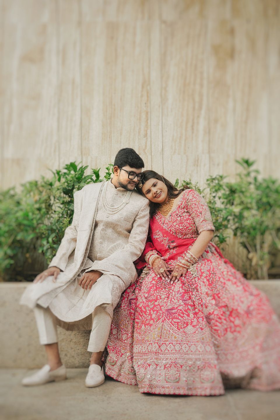 Couple seated together against a textured wall, the bride resting her head on his shoulder