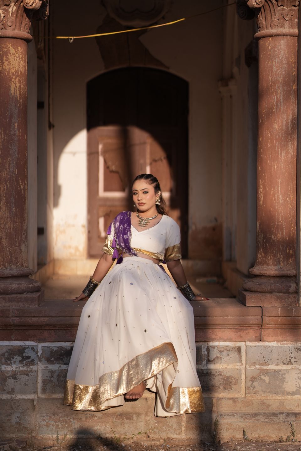 Model in a white and gold lehenga seated on heritage steps in evening light