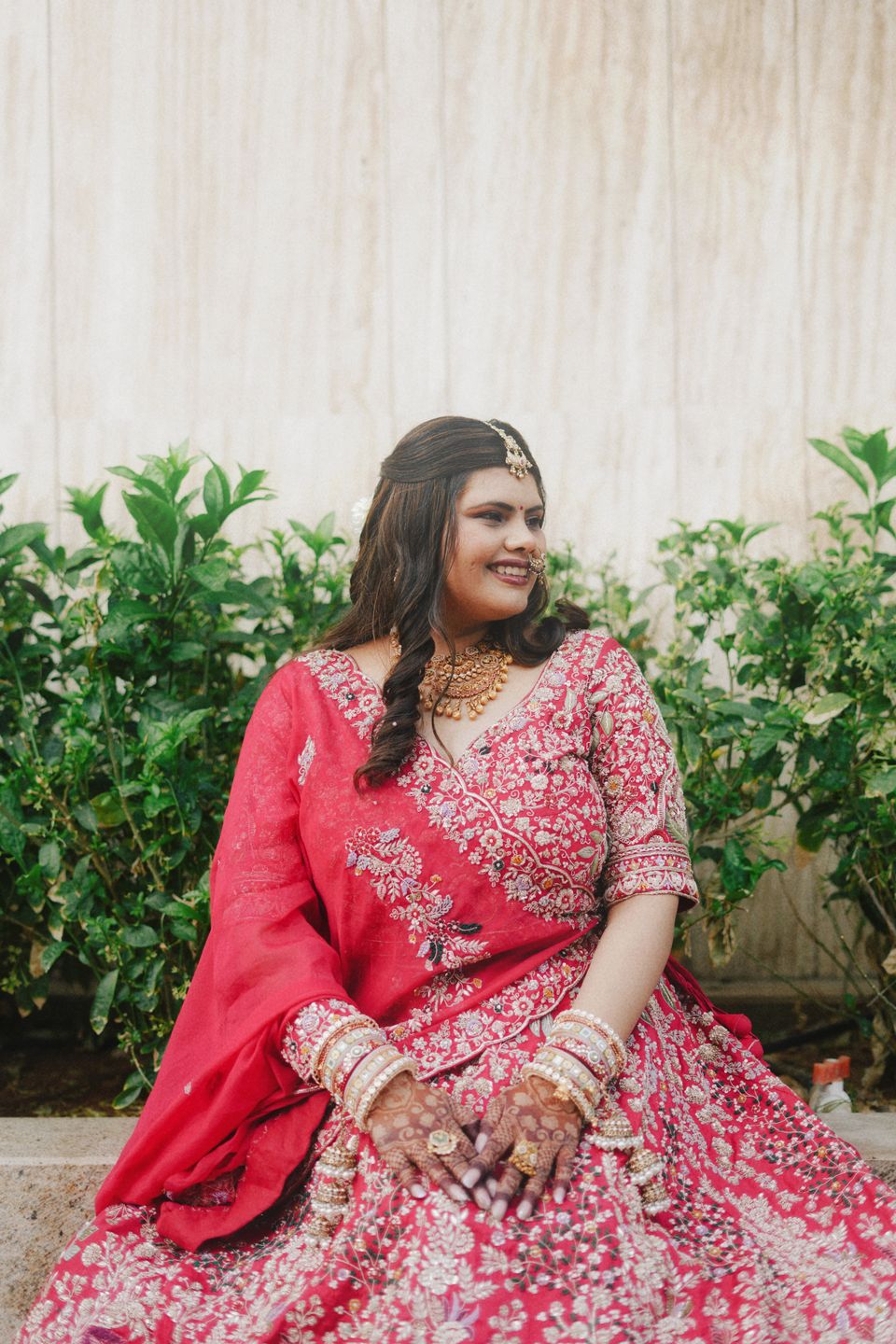 Bride in a pink and red lehenga seated in a garden, smiling