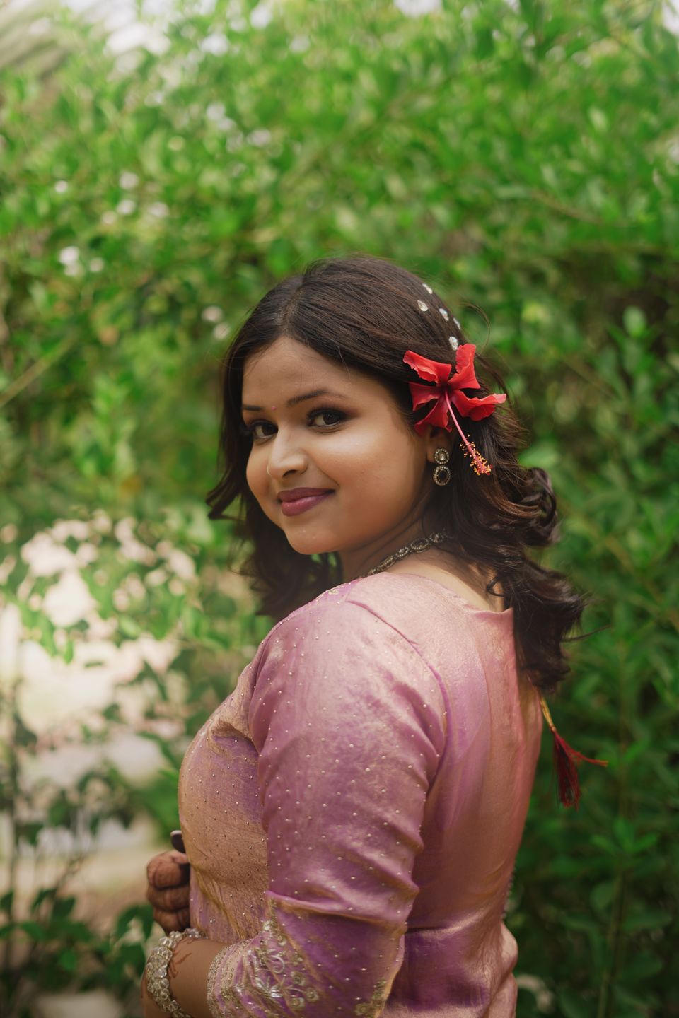 Woman in a pink saree with a red flower in her hair, looking over her shoulder