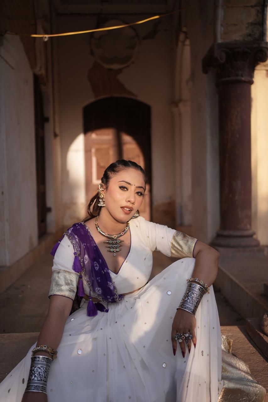 Model in white with silver jewellery seated in a sunlit heritage corridor