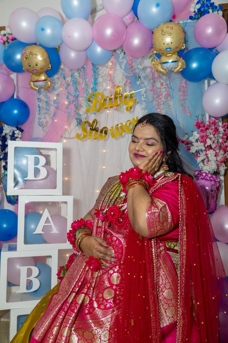 Mother-to-be in a red saree at a baby shower with balloons